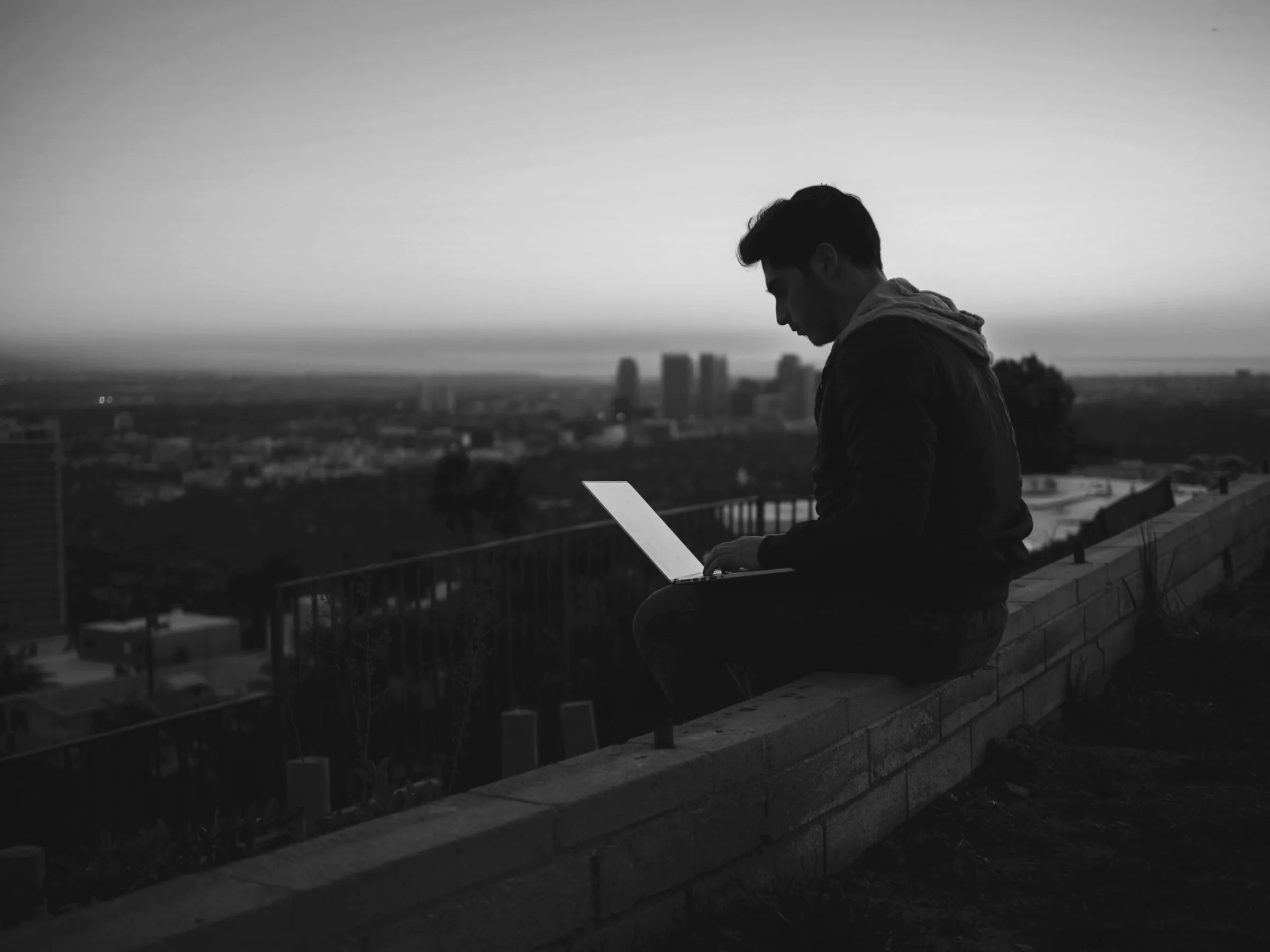 Working on a laptop at dusk above a city — the glowing screen the one persistent point as the session follows you on the go